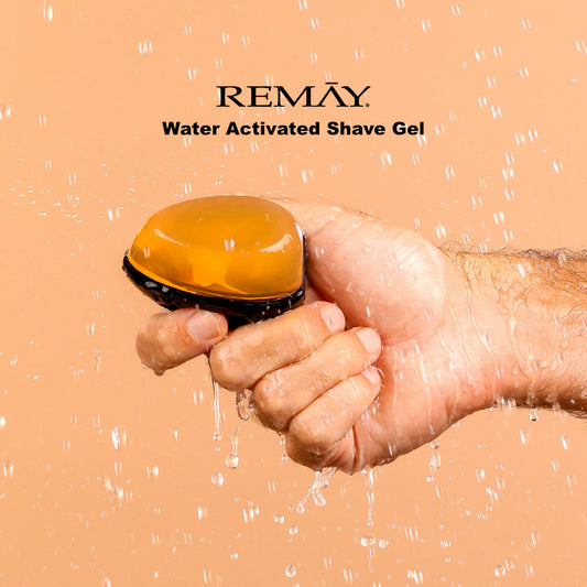 Hand holding an orange and black water activated shaving cream gel for men with REMAY branding on a beige background.
