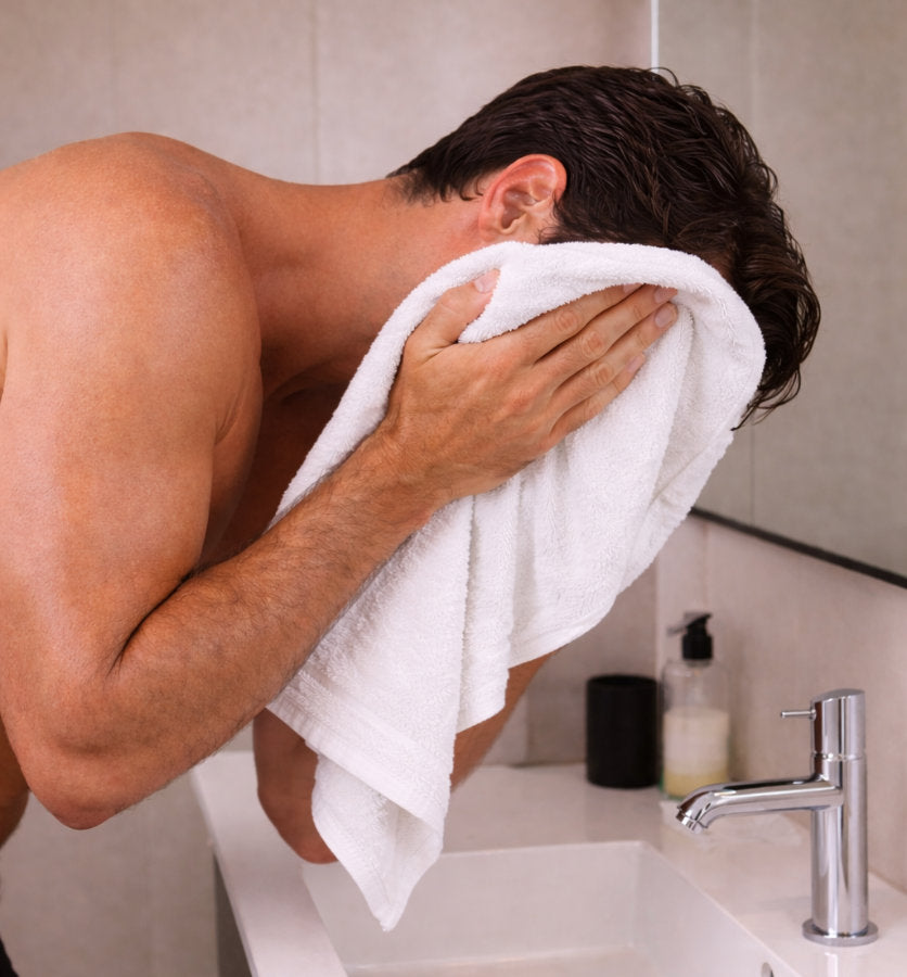 Man drying his face with a towel in a bathroom after shaving with REMAY shave gel.
