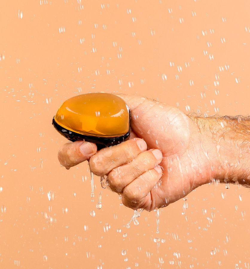 A mans hand holding the REMAY Heat shave gel bar with shower water falling on it.
