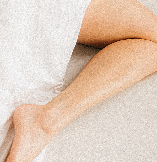 Close-up of a hairless female legs laying comfortably wrapped in bed sheets.
